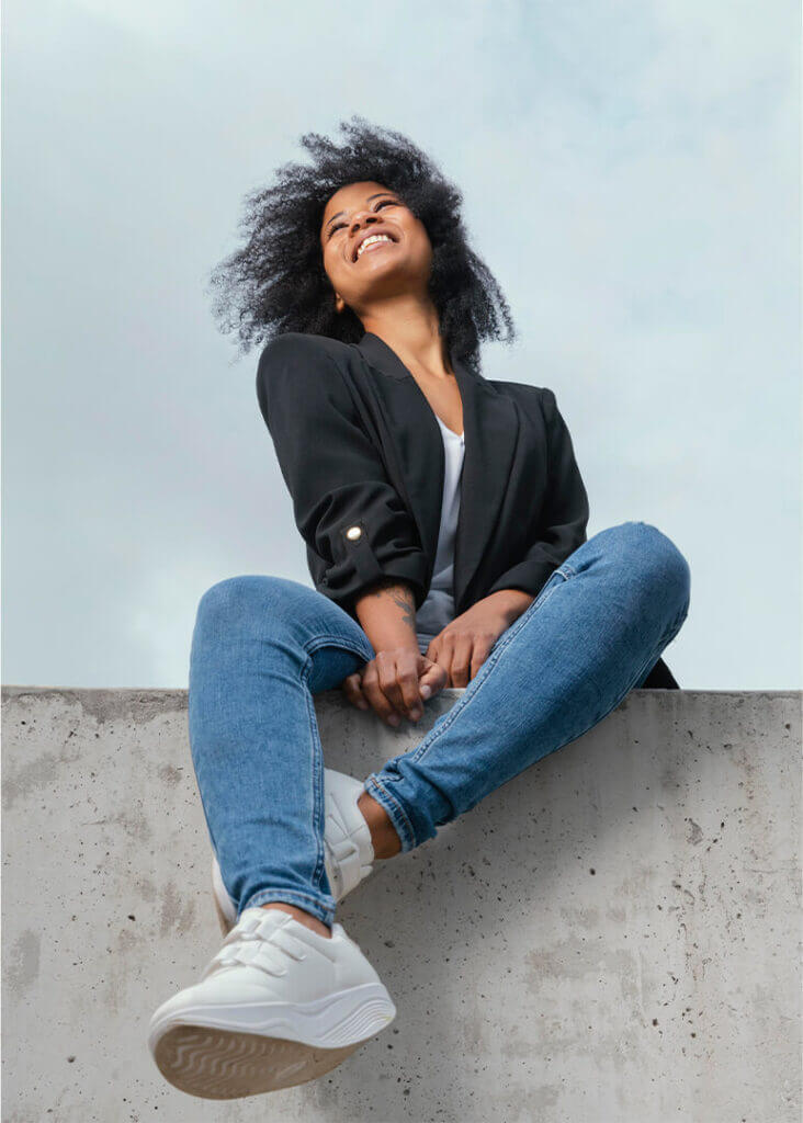 Chica sonriente sentada con su pantalón de jean y una chaqueta negra a juego